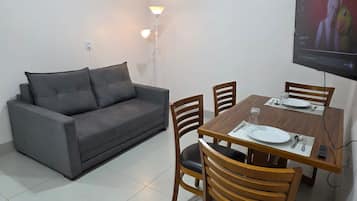Sala de estar com sofá, mesa de jantar, cadeiras e TV fixada na parede.