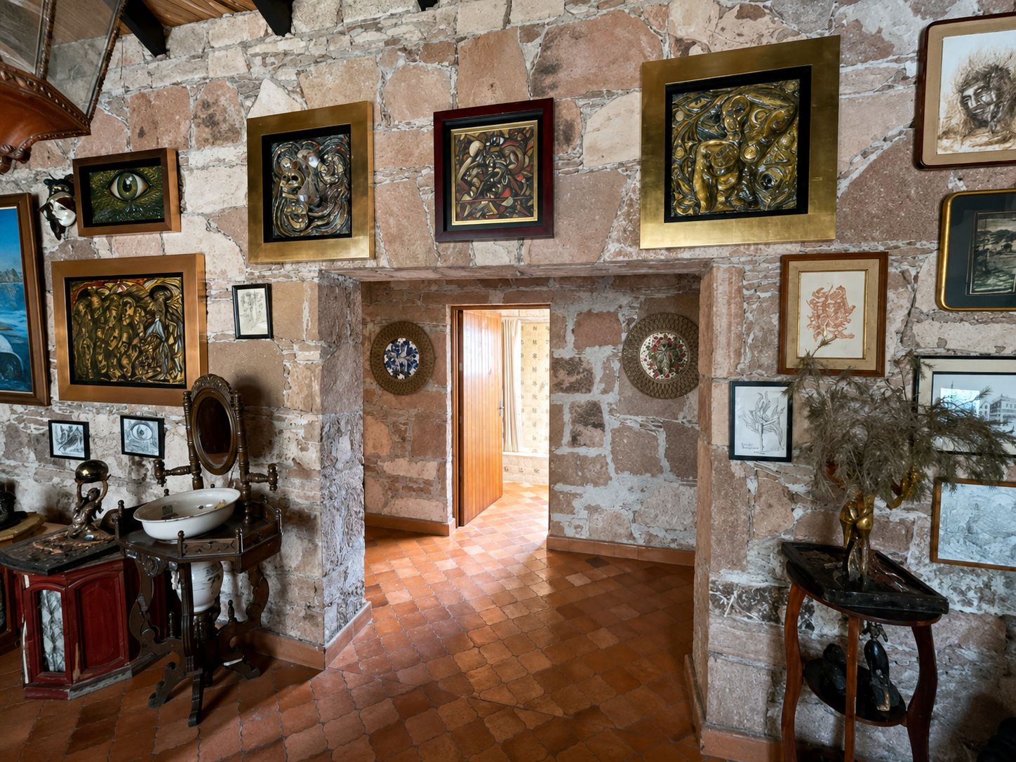Una habitación con paredes de piedra, suelo de baldosas y diversas obras de arte enmarcadas.