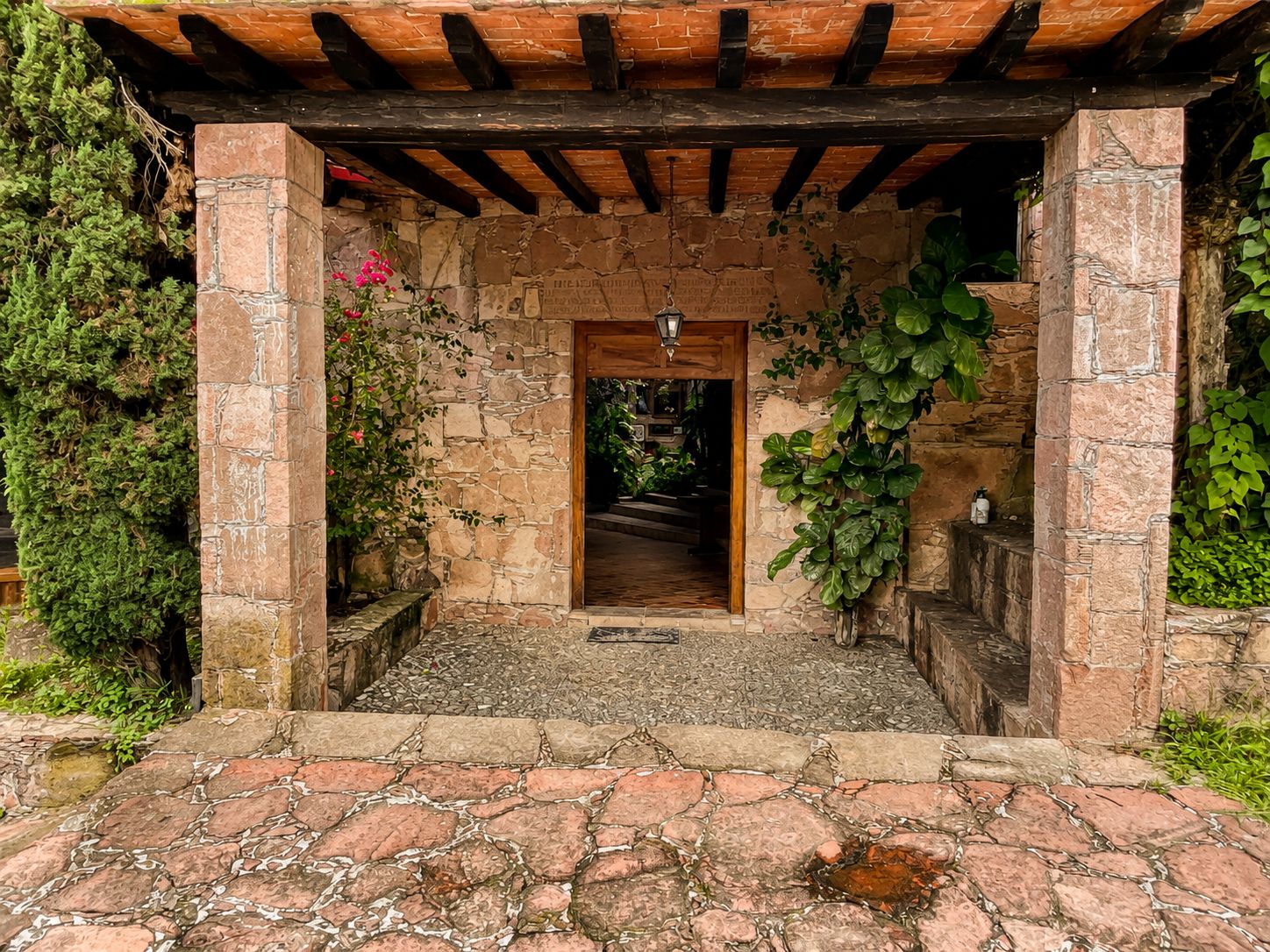 A stone archway leading to a wooden door, surrounded by greenery and stone paving.