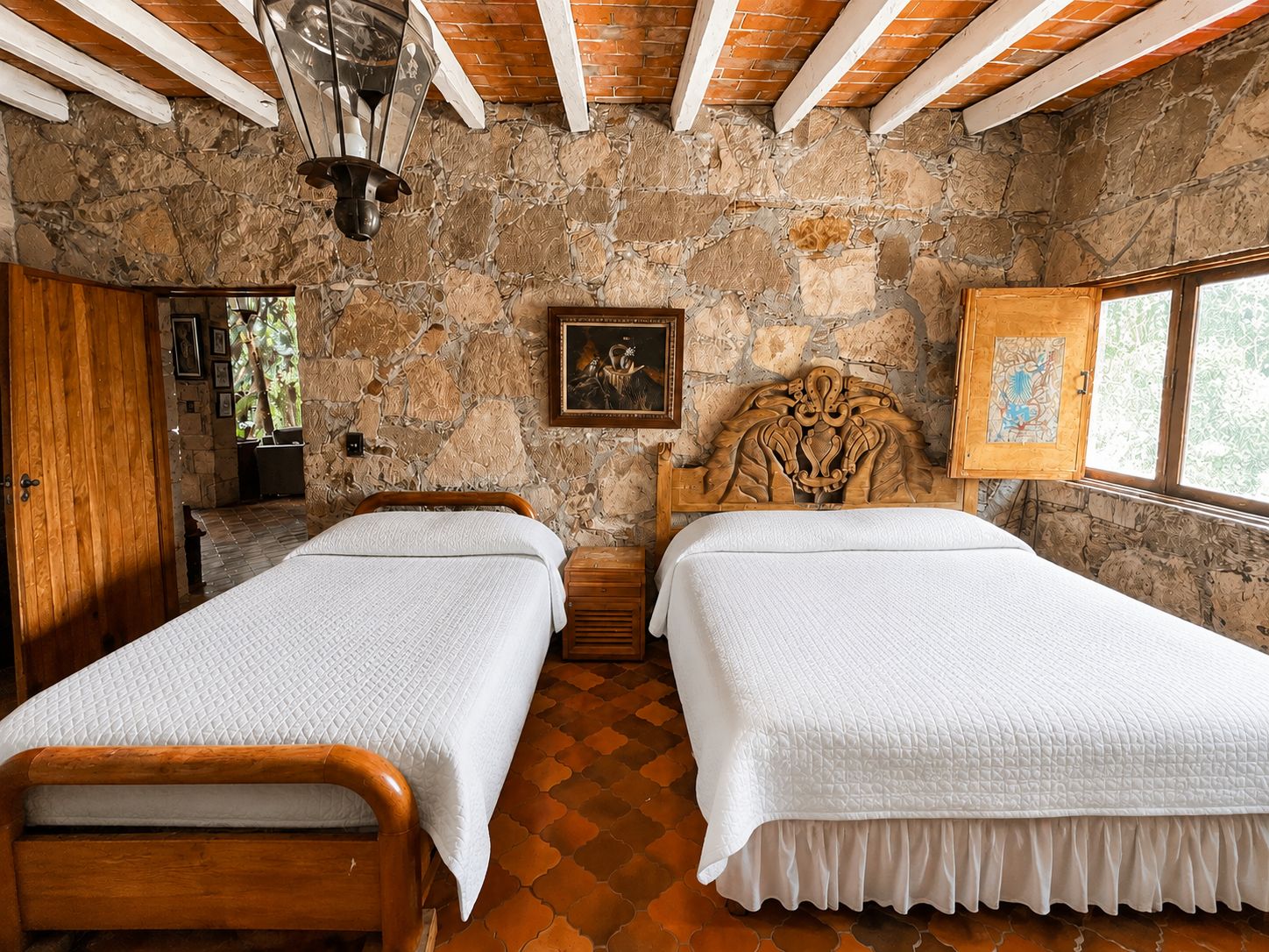 Una habitación con dos camas de madera, una pared de piedra, techo de madera y una ventana.