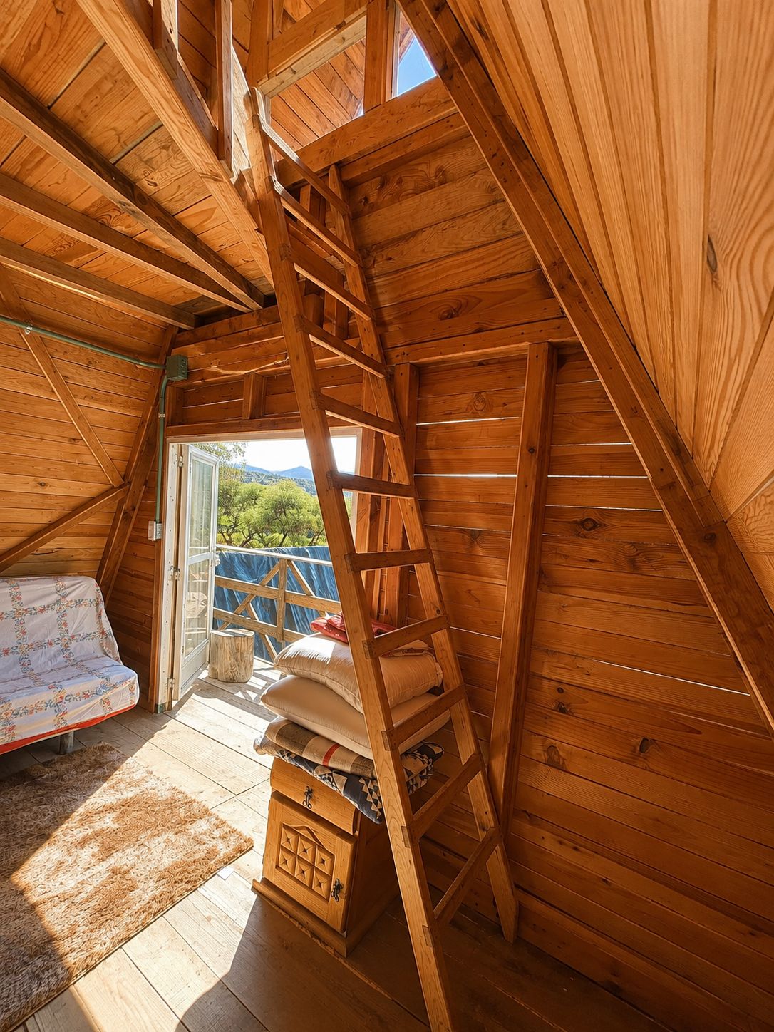 A wooden interior with a loft bed, a ladder, and a small storage chest.