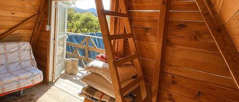 A wooden interior with a loft bed, a ladder, and a small storage chest.