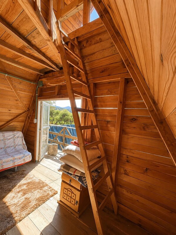 A wooden interior with a loft bed, a ladder, and a small storage chest.