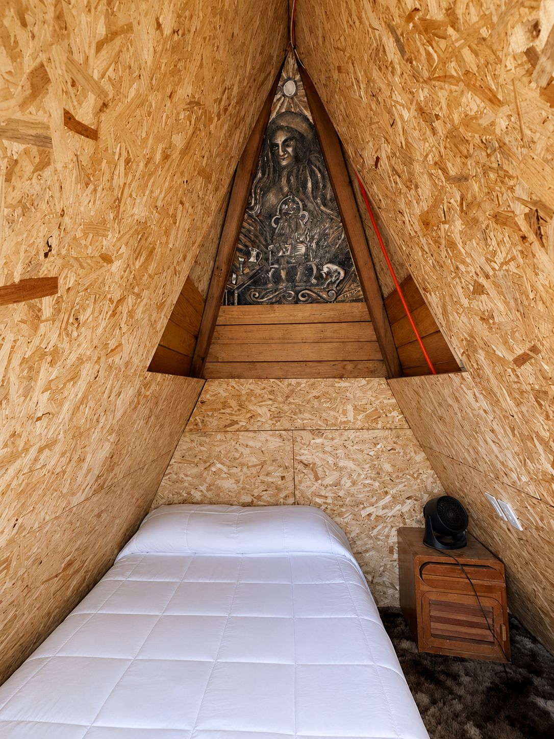 Un dormitorio pequeño y triangular en el ático, con techo inclinado de madera, una cama y un adorno en la pared.