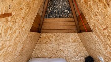 Un dormitorio pequeño y triangular en el ático, con techo inclinado de madera, una cama y un adorno en la pared.