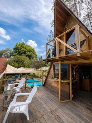 A wooden cabin with a deck, outdoor seating, and a pool.
