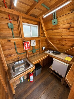 A compact wooden cabin with a kitchenette, a window, and a fire extinguisher.