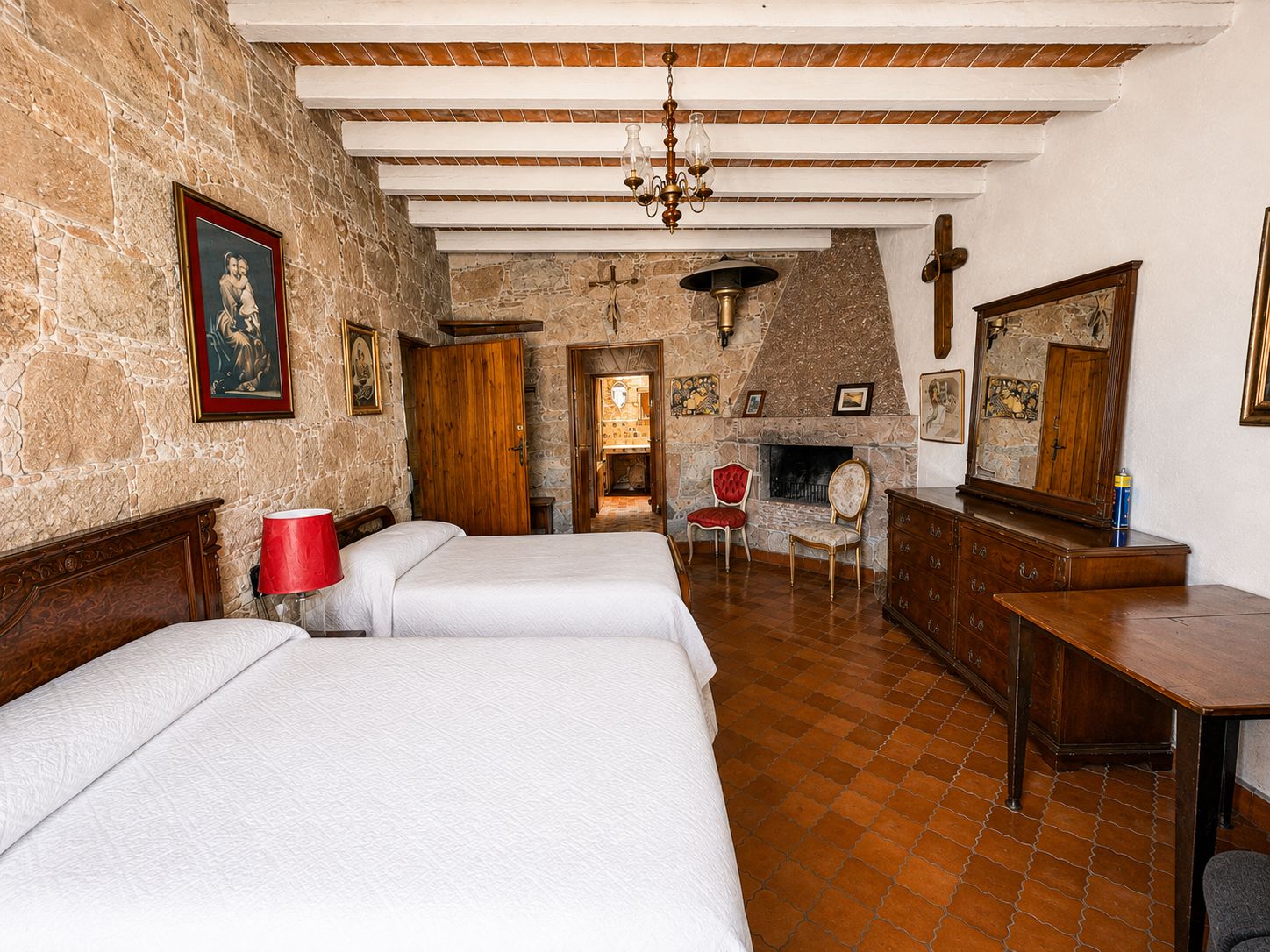 A room with a stone wall, wooden beams, a fireplace, a bed, a chair, and a dresser.
