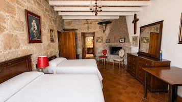 A room with a stone wall, wooden beams, a fireplace, a bed, a chair, and a dresser.