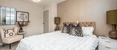 Un dormitorio con una cama grande, una mesita de noche, una lámpara, una silla y una pared con textura.