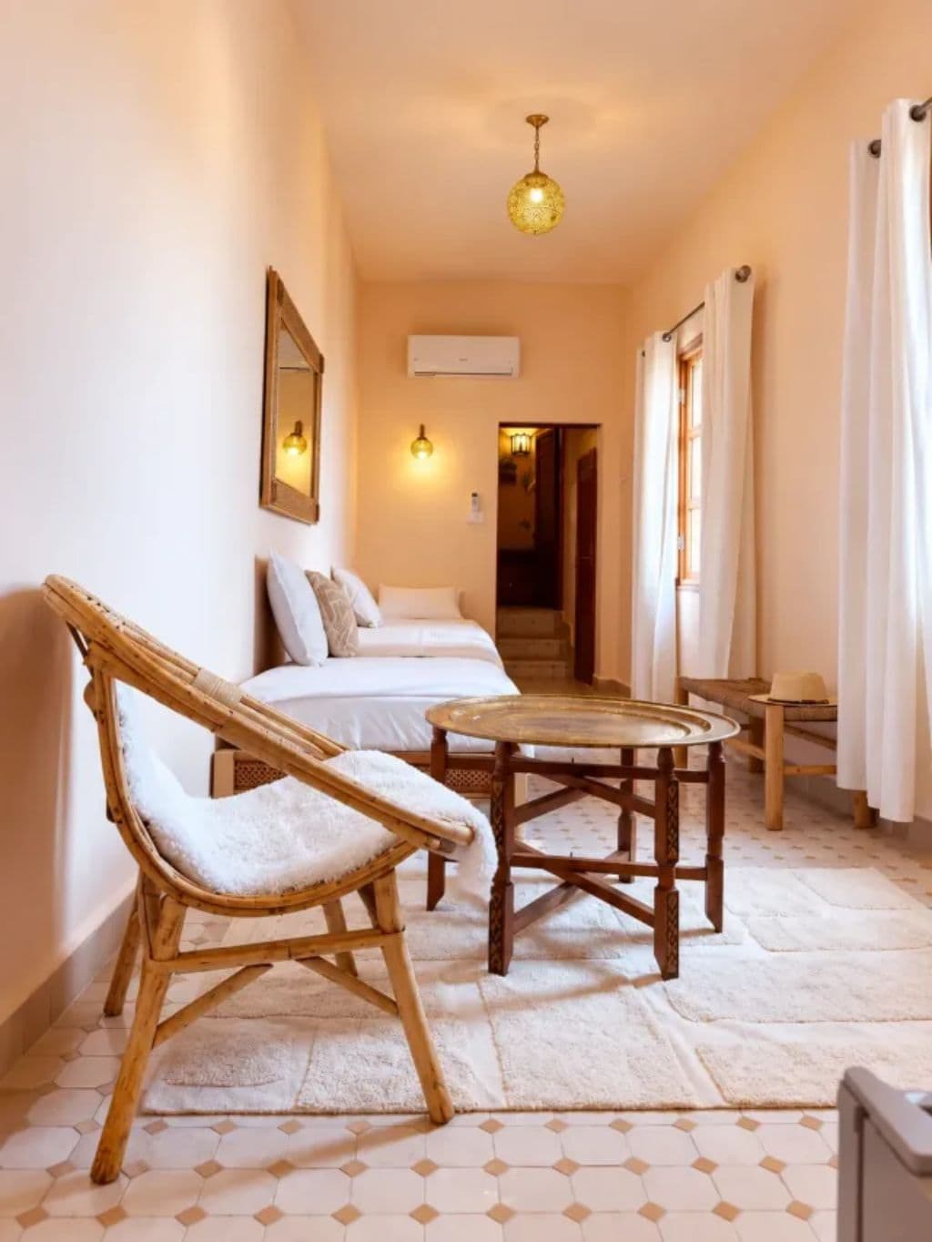 A corridor with a bed, a chair, a table, and a hanging light fixture.