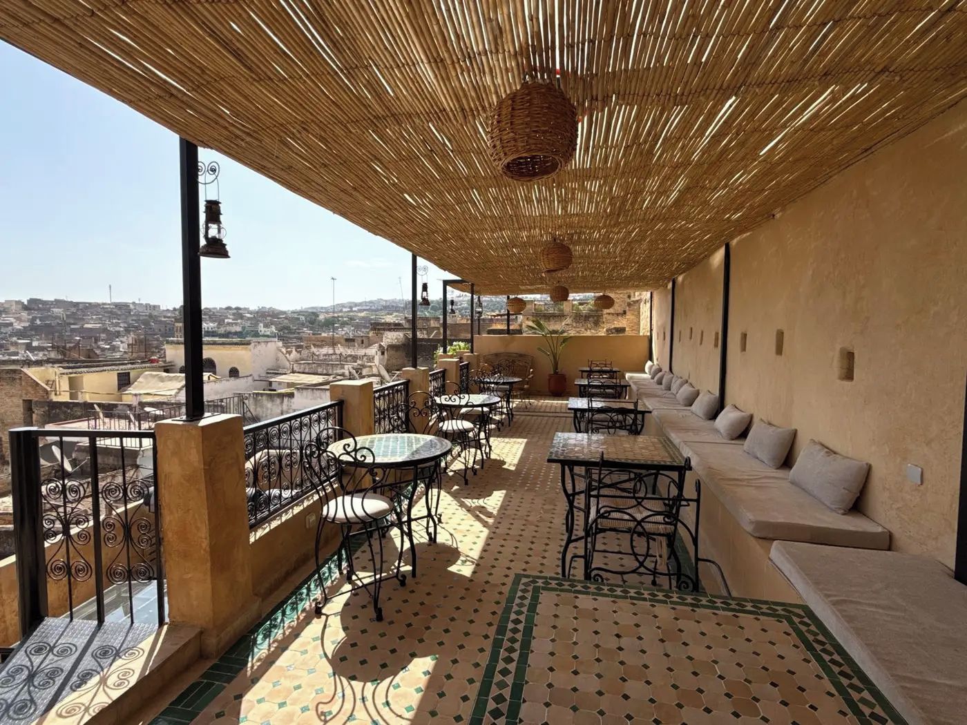 A rooftop terrace with outdoor seating, a view of the city, and a thatched roof.