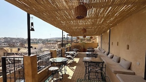 Una terraza en la azotea con mobiliario exterior, vistas de la ciudad y un techo de paja.