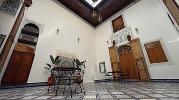 A room with a tiled floor, a central table, and a hanging light fixture.