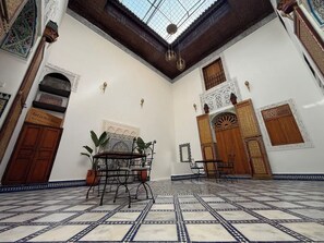 A room with a tiled floor, a central table, and a hanging light fixture. - Riad La Petite Maison (Fès)