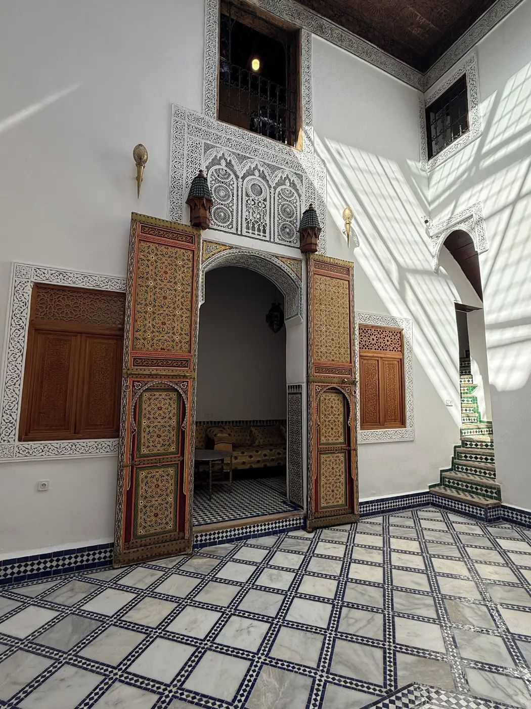 Un interior con puertas ornamentadas, un suelo a cuadros y una escalera.