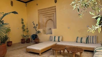 Una habitación con sofá, dos mesas de madera, un colchón y plantas en macetas.