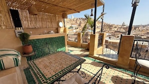 Una terraza en la azotea con una mesa, sillas, una planta en maceta y vistas de la ciudad.