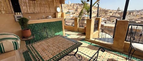 Terraço no telhado com mesa e cadeiras, um vaso de planta e vista para a paisagem urbana.