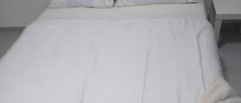Una cama con ropa de cama blanca y una manta blanca.