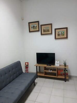 A living room with a dark blue sofa, a television on a wooden stand, and three framed pictures on the wall.