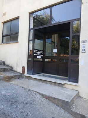 Entrada de un edificio con un amplio escaparate de vidrio, una escalera de emergencia metálica y un pequeño espacio exterior con escalones.