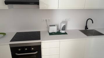 A modern kitchen with white cabinets, a black dishwasher, a built-in oven, a stainless steel sink, and a toaster.