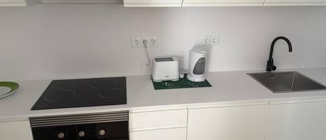 Una cocina moderna con armarios blancos, un lavavajillas negro, horno empotrado, pileta de acero inoxidable y un tostador.