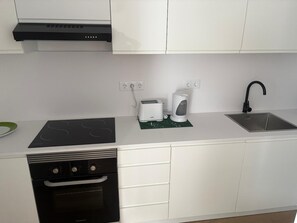 A modern kitchen with white cabinets, a black dishwasher, a built-in oven, a stainless steel sink, and a toaster.