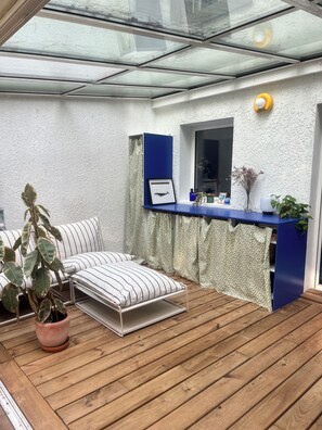 A sunroom with a wooden deck, a sofa, a small table, and a potted plant. - Three-bedroom house with a garden overlooking the forest. Quiet neighborhood, near a bike path (Capbreton)