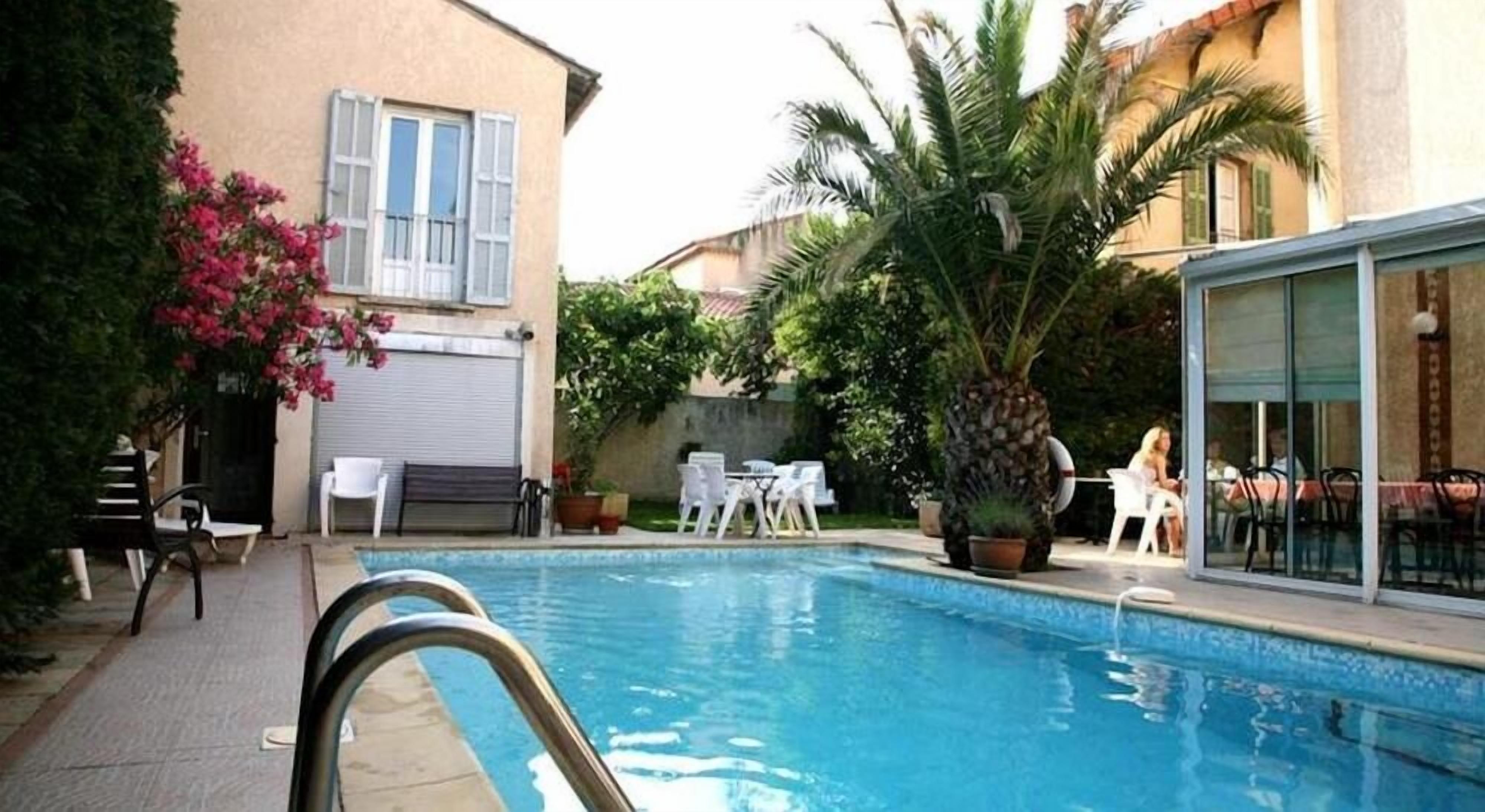 Une piscine avec un espace patio, des sièges d’extérieur et un bâtiment doté de volets.