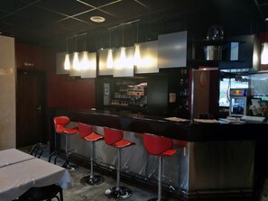 Un espace bar avec un comptoir, des tabourets de bar rouges, des suspensions décoratives et un réfrigérateur orné du logo Red Bull.