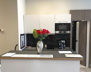 A modern kitchen with white cabinets, a Bosch microwave, and a vase with red flowers on the counter. - Verde Design Apartment (Bad Camberg)