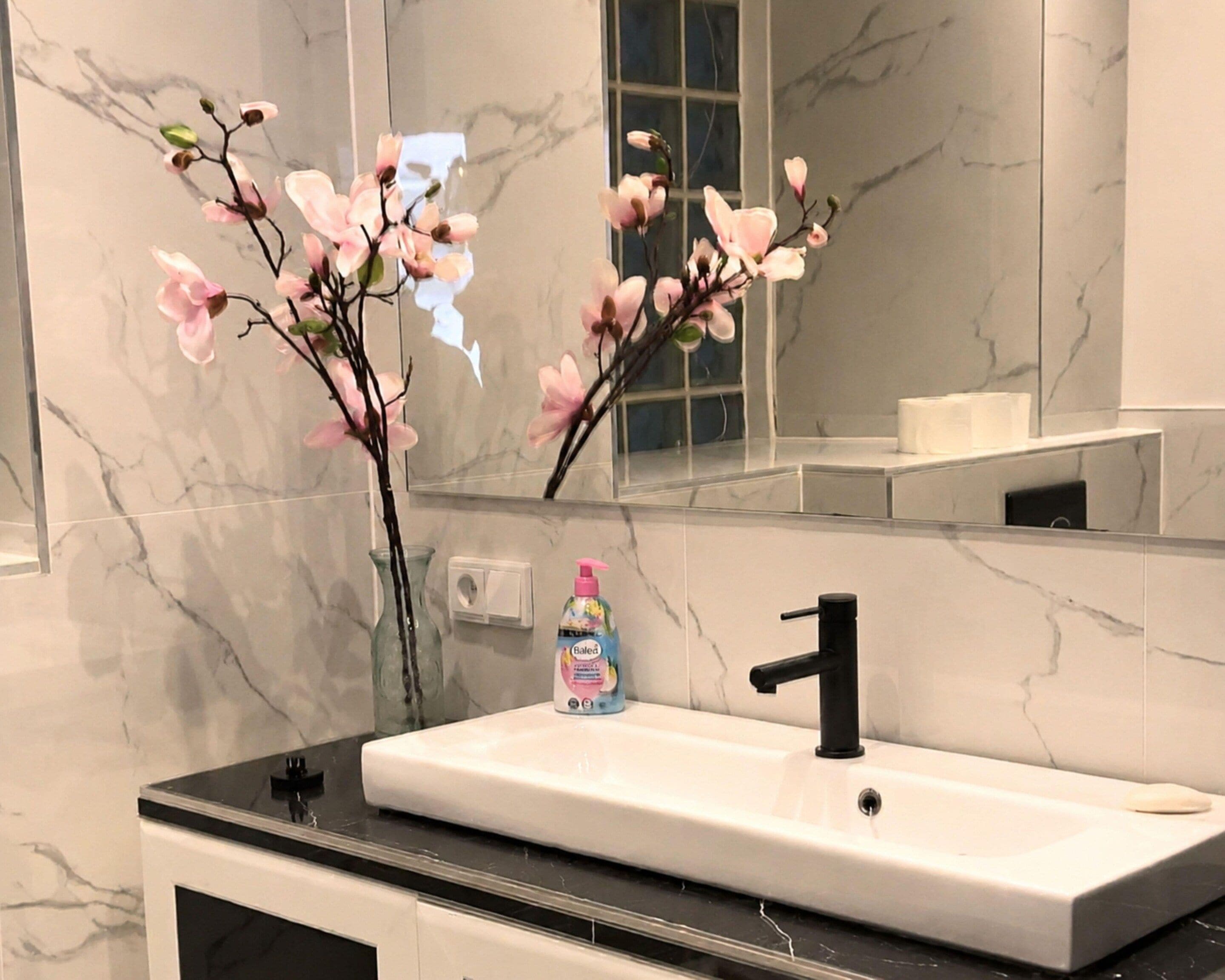 A bathroom with a white sink, black faucet, and a vase with pink flowers.