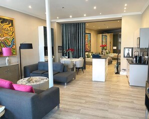Ein modernes Wohnzimmer mit einem grauen Sofa, einem Couchtisch und einem Essbereich mit einem weißen Tisch und Stühlen.