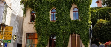 A building covered in ivy with a traditional facade, a staircase leading to the entrance, and a clear sky above.