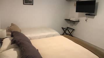A hotel room with two beds, a flat-screen TV mounted on the wall, a small table with a lamp, and a framed picture on the wall.