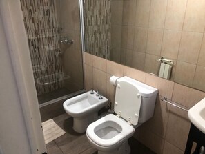 A bathroom with a bidet, toilet, and shower.