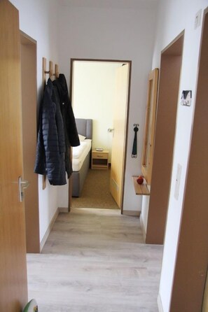 A narrow hallway with wooden doors on either side, leading to a room with a bed and a small table. - The Nordwind vacation rental is located in the heart of Dornumersiel (Dornumersiel)