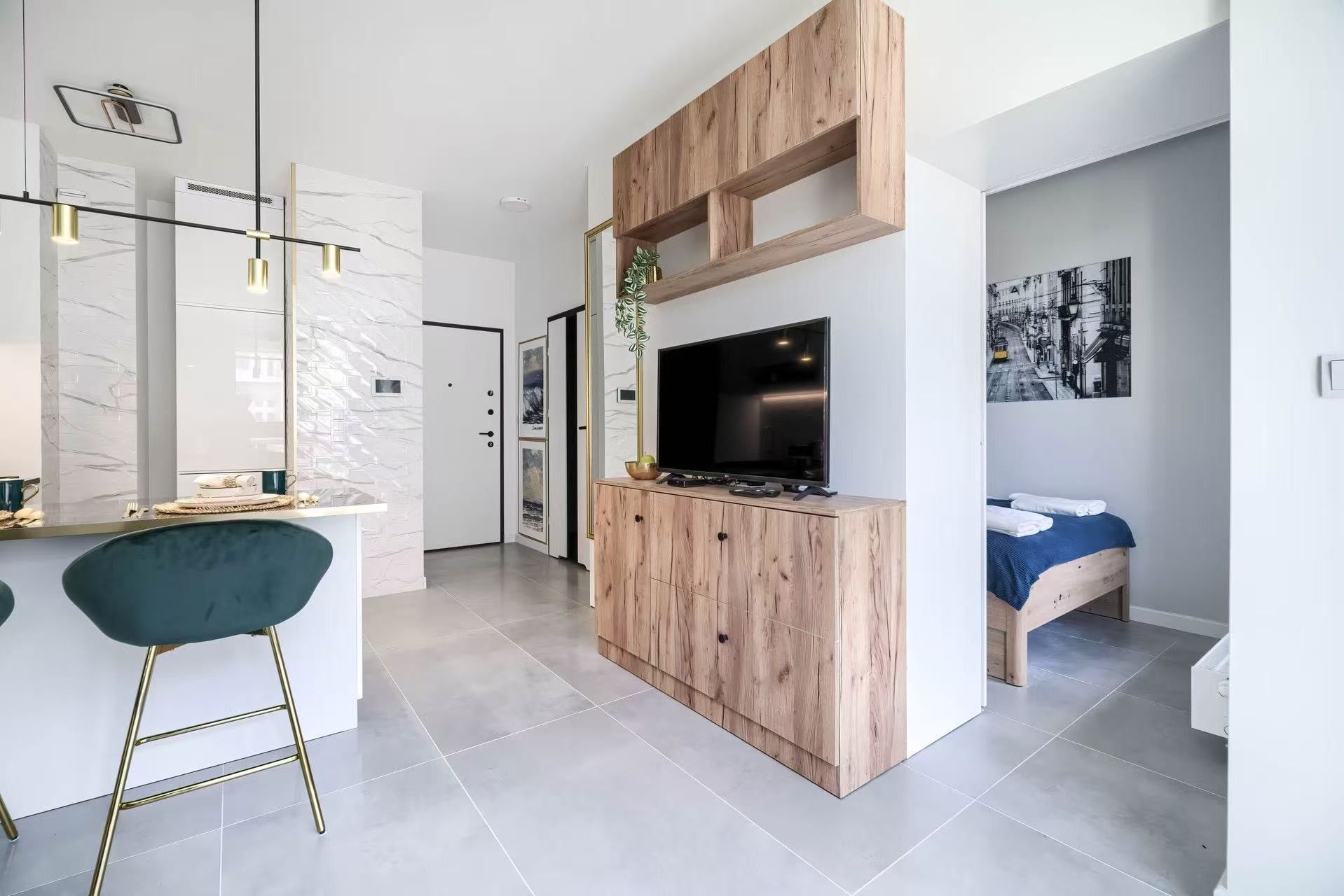 A modern living space with a kitchen area, a dining table with chairs, a TV mounted on a wooden cabinet, and a bed with a blue blanket.