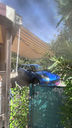 A blue car parked in a driveway with a wooden fence and a metal gate. - Stunning, fully equipped mobile home in a very quiet community (Sainte-Maxime)