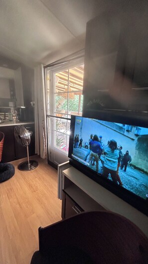 A living room with a flat-screen TV mounted on a stand, a dining area with a table and chairs, and a window with curtains. - Stunning, fully equipped mobile home in a very quiet community (Sainte-Maxime)