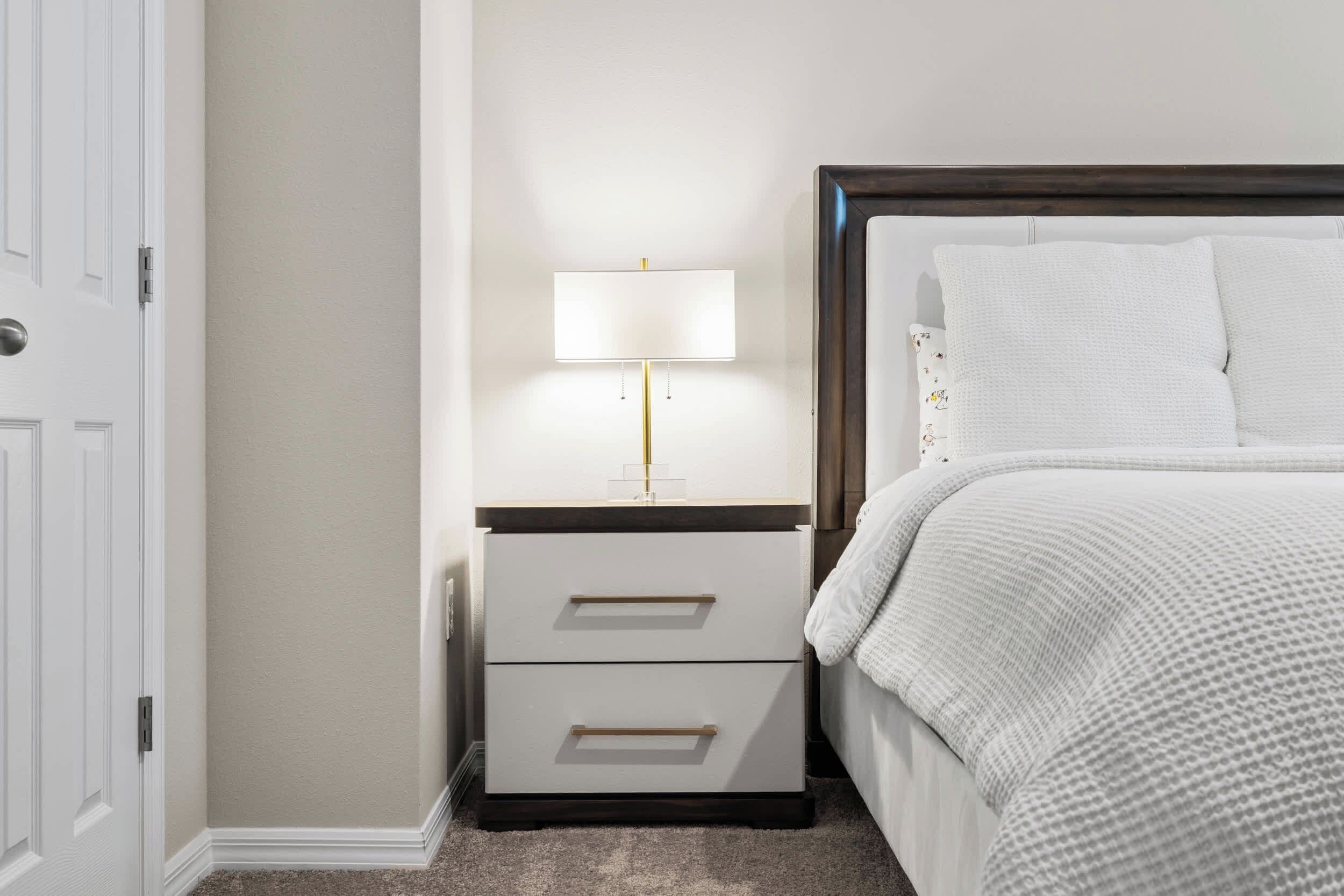 Une chambre à coucher avec un lit, une table de chevet avec une lampe et une porte.