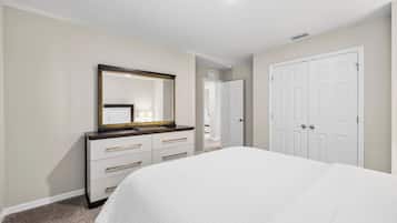 Un dormitorio con cama, cómoda con cajones, espejo y puerta.