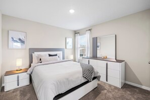 Un dormitorio moderno con una cama, mesitas de noche, un tocador y un espejo grande.