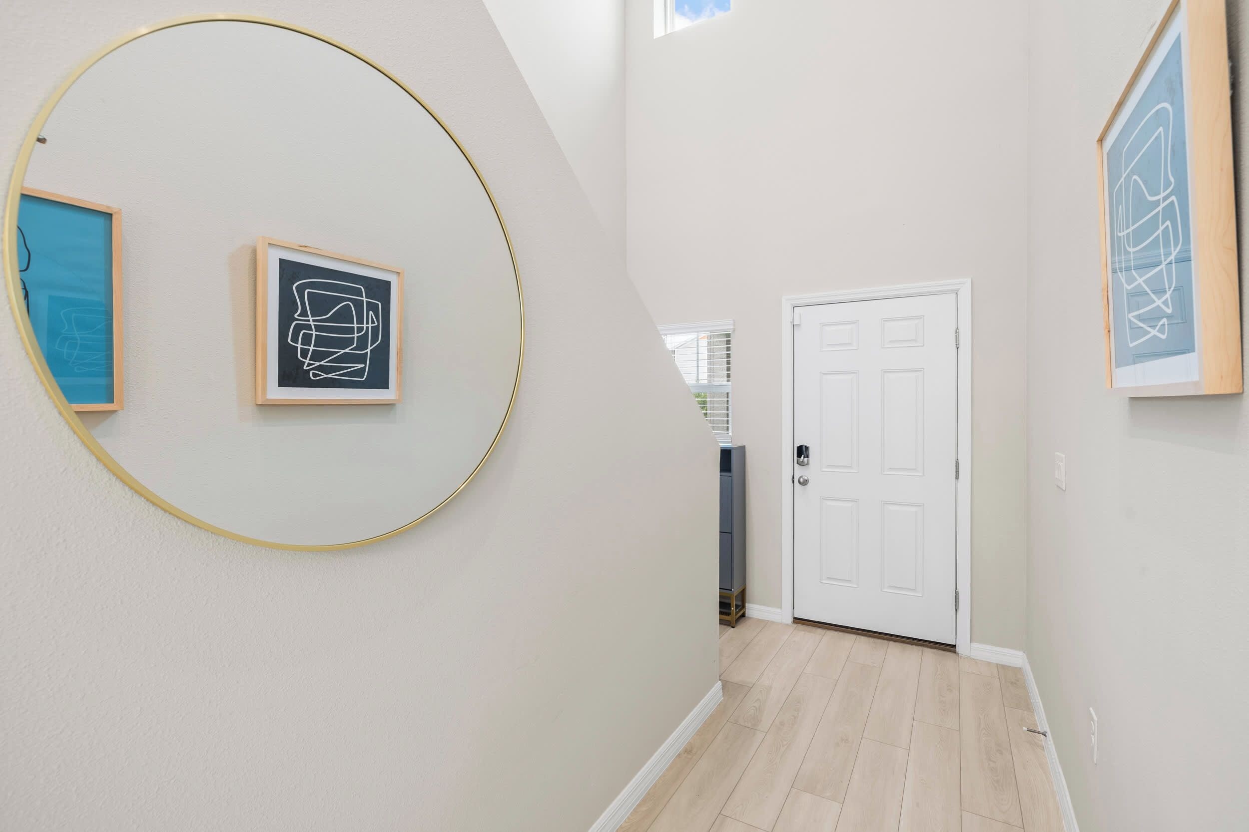 A hallway with a white door, a framed abstract artwork, and a circular frame on the wall.