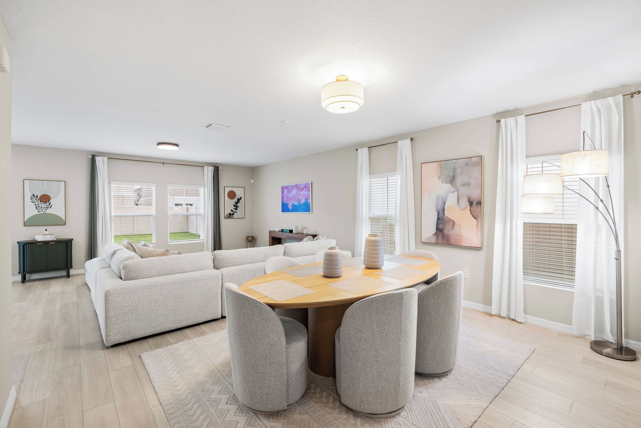 A modern living room with a sectional sofa, a round dining table with chairs, and artwork on the walls.