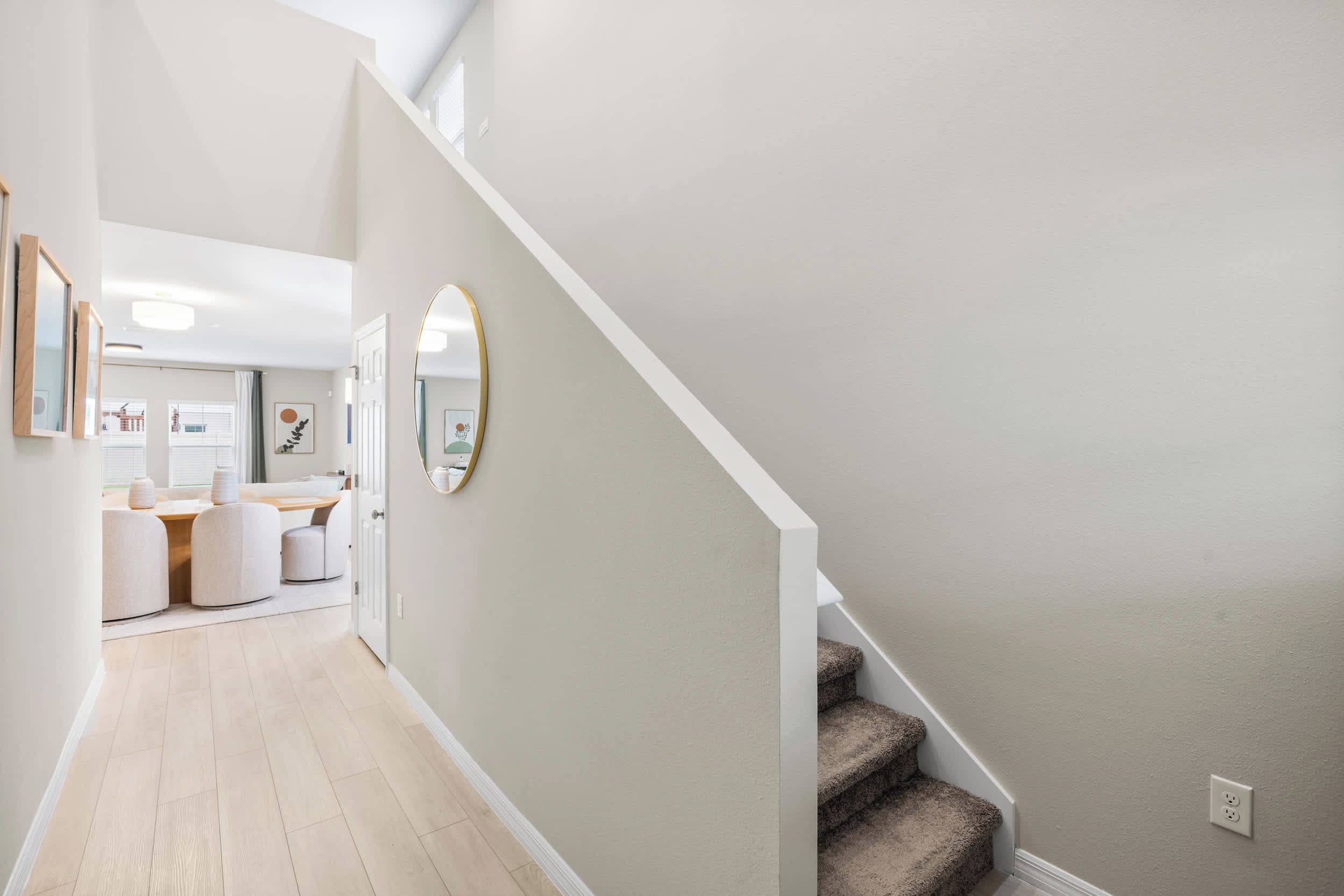 A hallway with a staircase leading to a bedroom, a dining area with a table and chairs, and a bathroom with a toilet and sink.