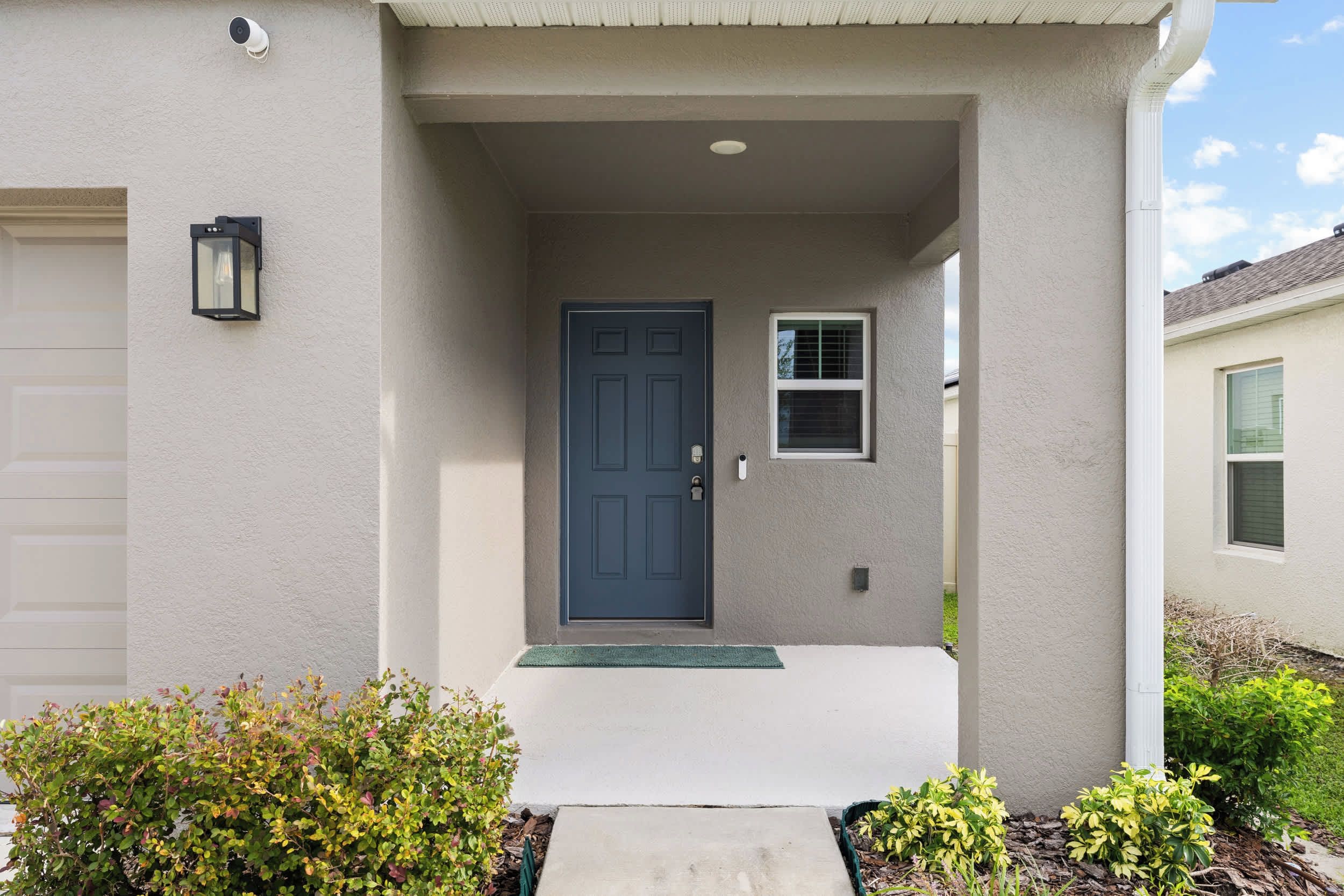 A residential house with a dark blue front door, a small window, and a security camera.