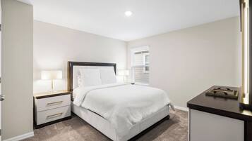 A bedroom with a bed, bedside tables, a nightstand, a window with blinds, and a mirror.